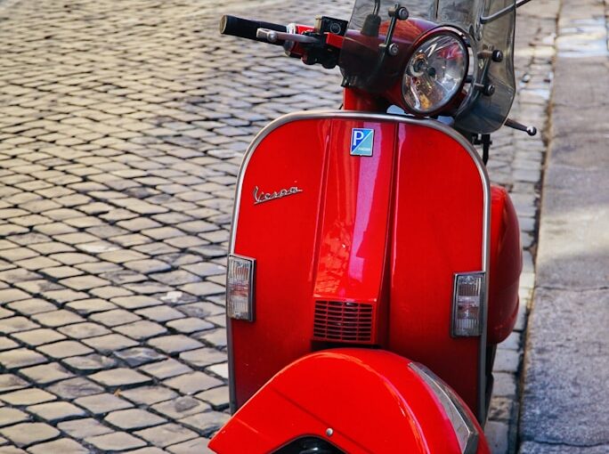 red motor scooter parked on gray brick pavement